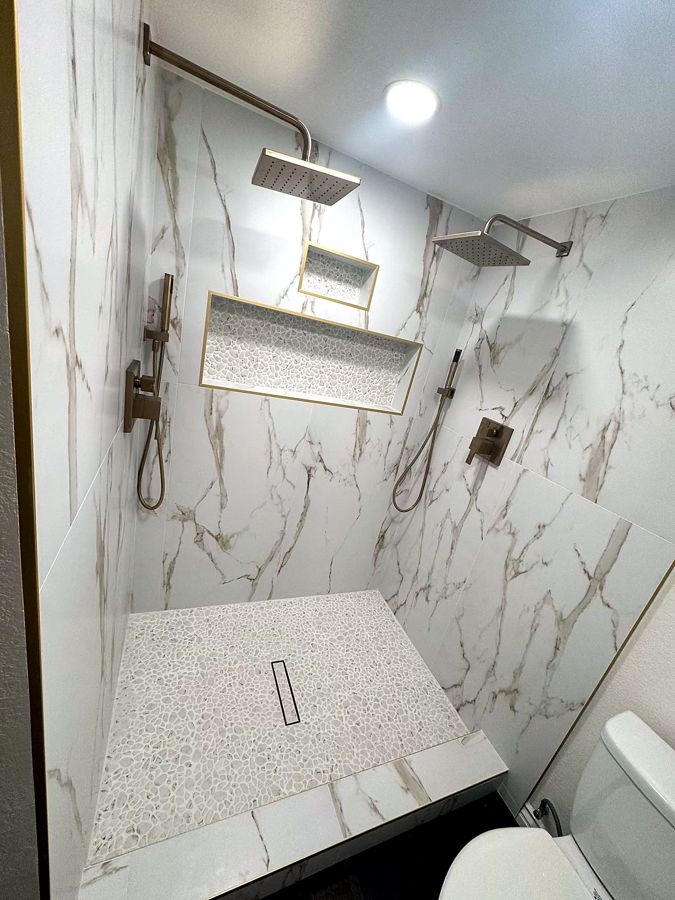 Marble walk-in shower with dual brushed-gold rainfall heads and pebble-stone floor