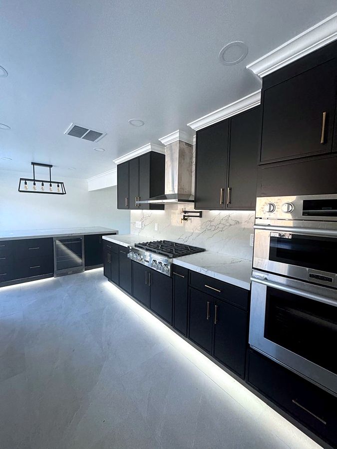 Matte-black kitchen with marble backsplash, stainless hood, and under-cabinet lighting