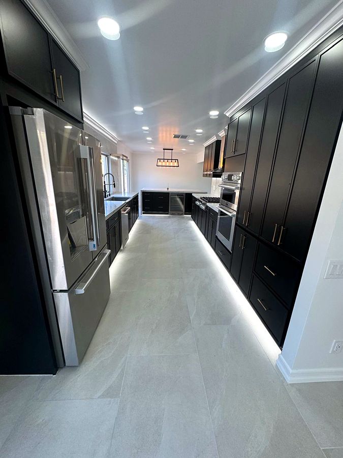 Galley view of remodeled kitchen with dark cabinets and light stone floors